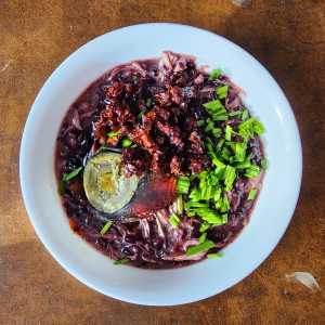 A bowl of black rice congee with century egg, scallions, and chili crisp